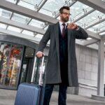 Young man checking his watch and pulling suitcase
