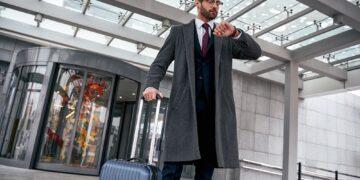 Young man checking his watch and pulling suitcase