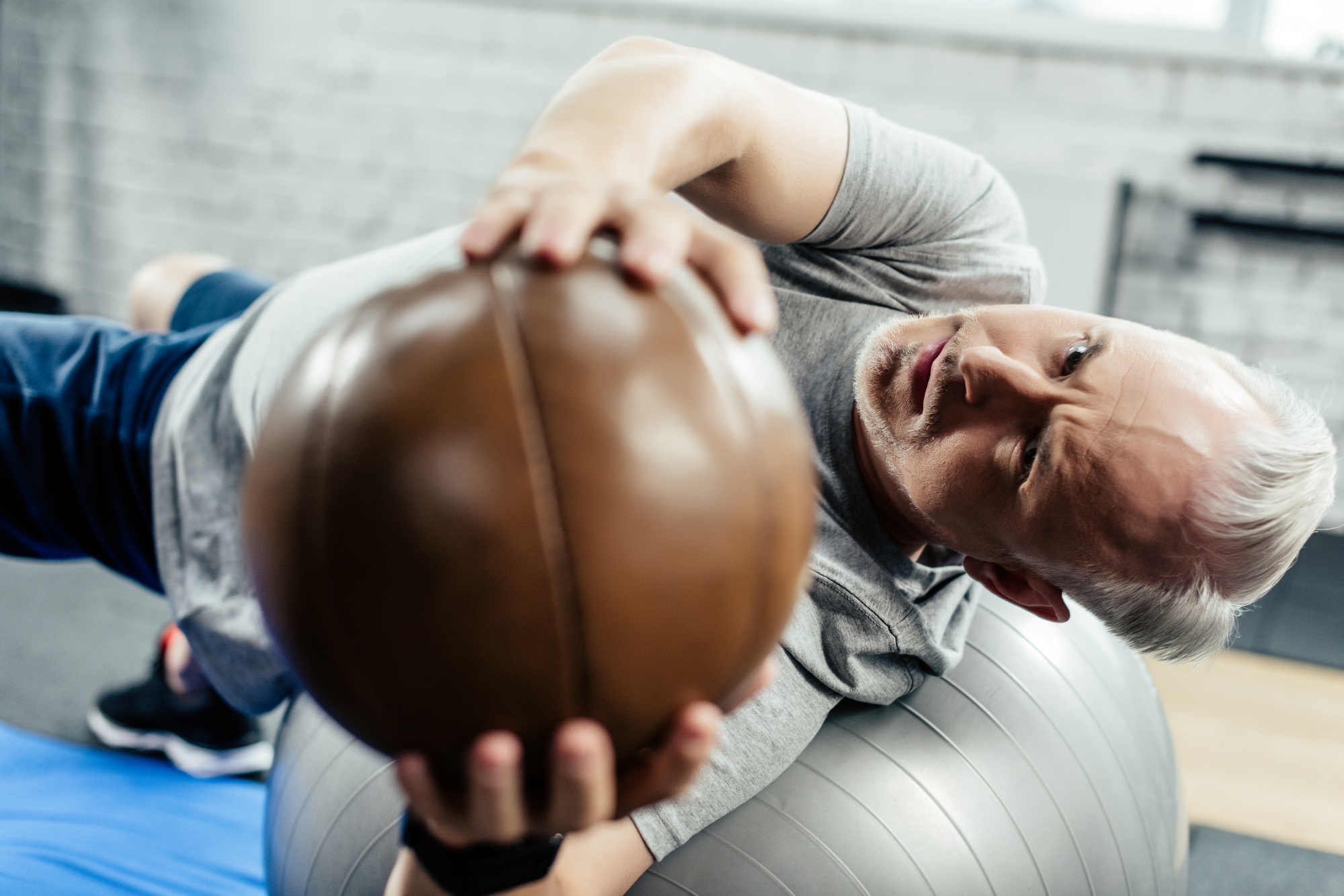 senior sportsman training on on fitness ball with medicine ball in gym