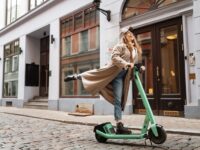 Young blonde woman riding a kick scooter in city street