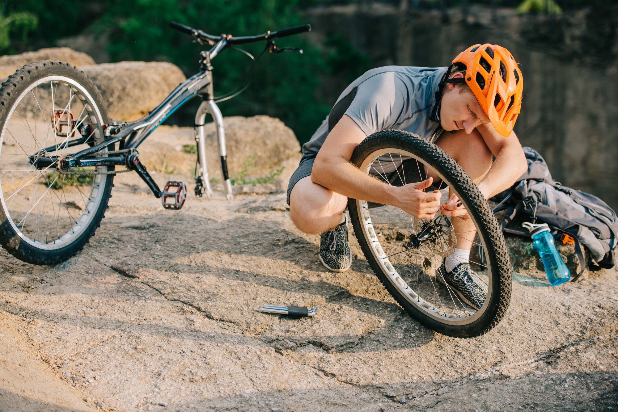 young trial biker fixing bike wheel outdoors
