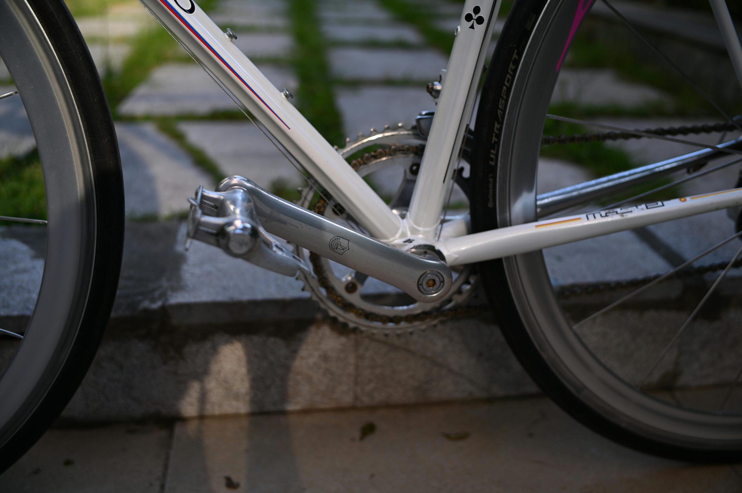 Detailed view of a road bicycle's crankset and pedals on a stone path, outdoors.