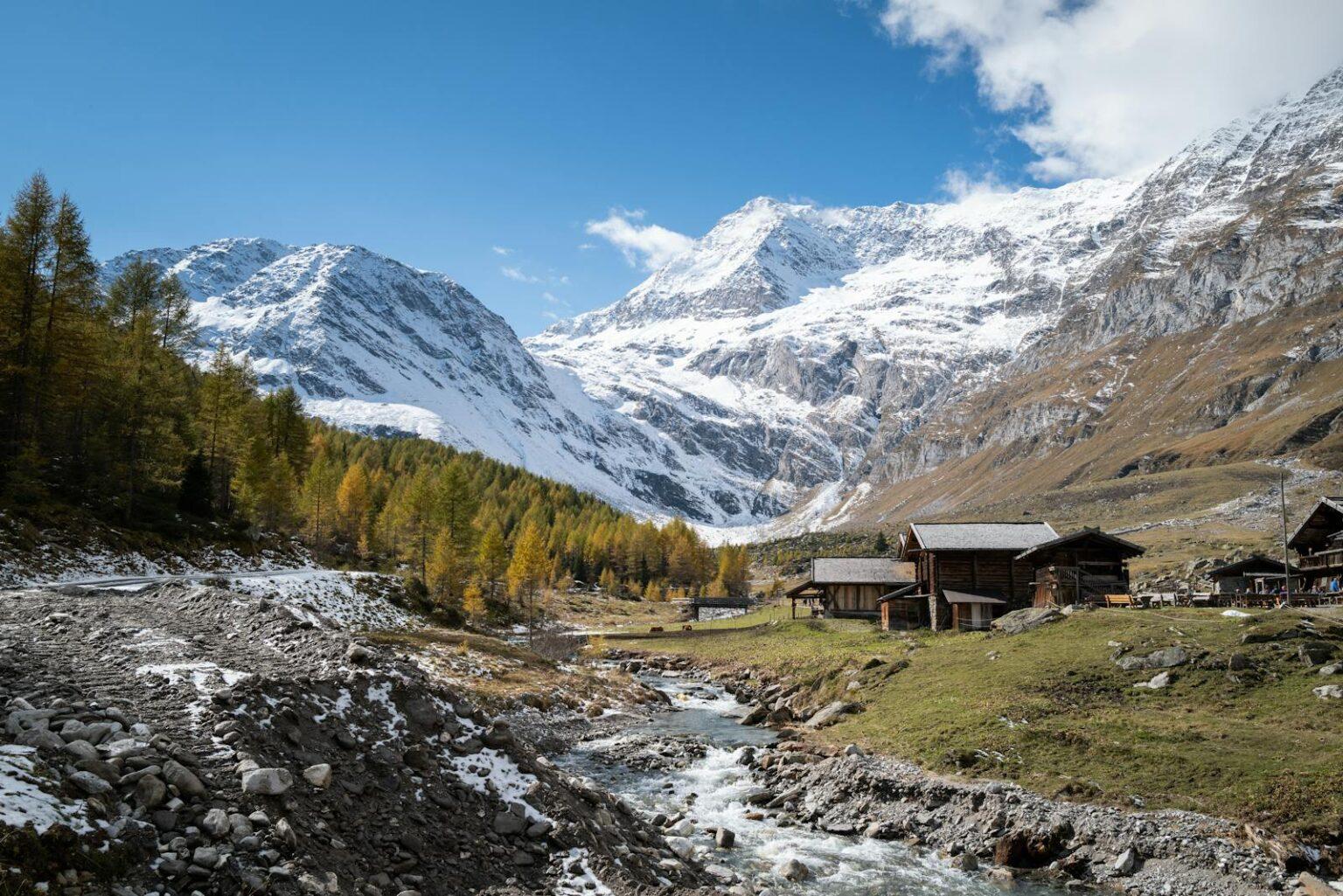 Charming alpine village with rustic cabins and snow-capped mountains under clear blue skies.