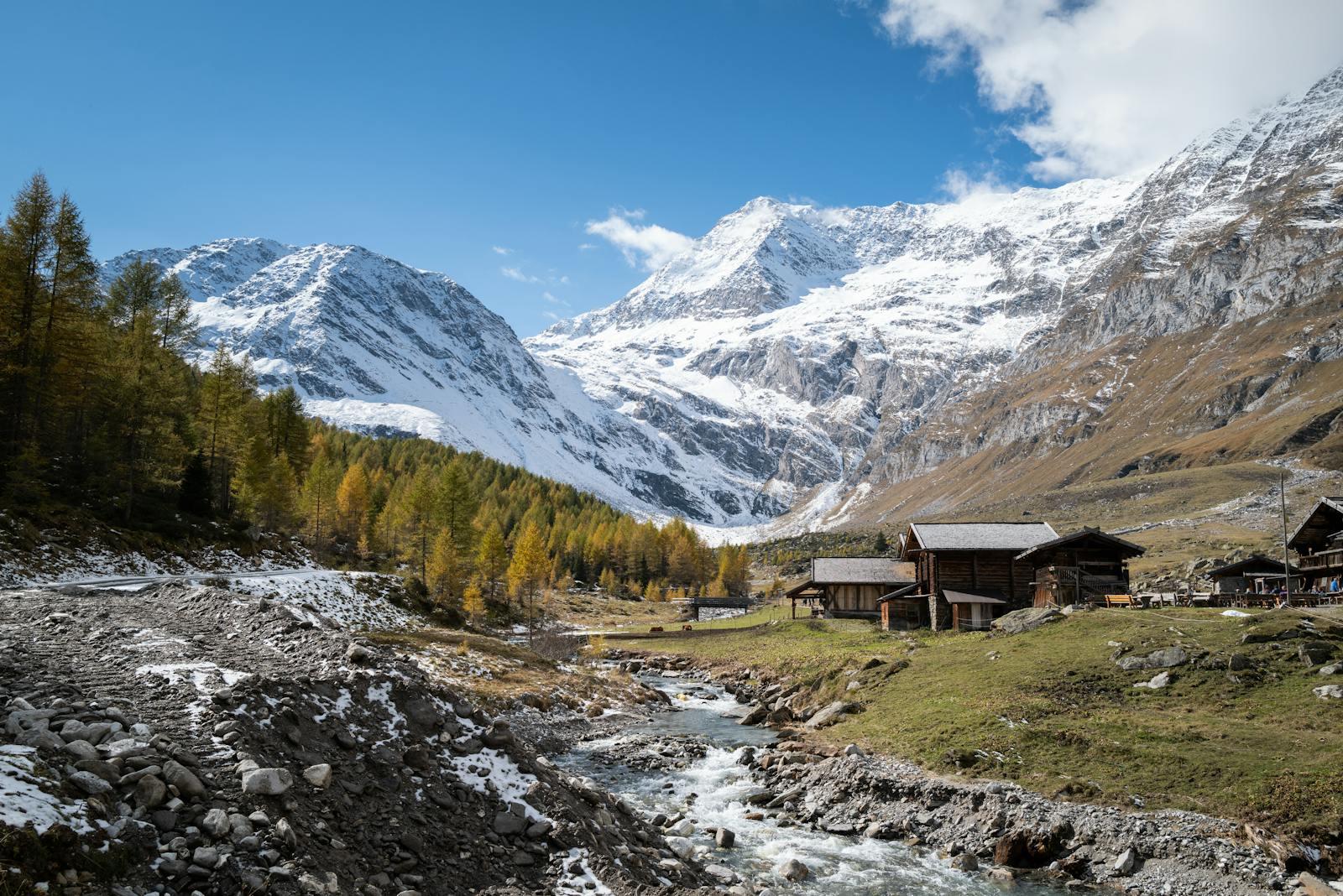 Charming alpine village with rustic cabins and snow-capped mountains under clear blue skies.