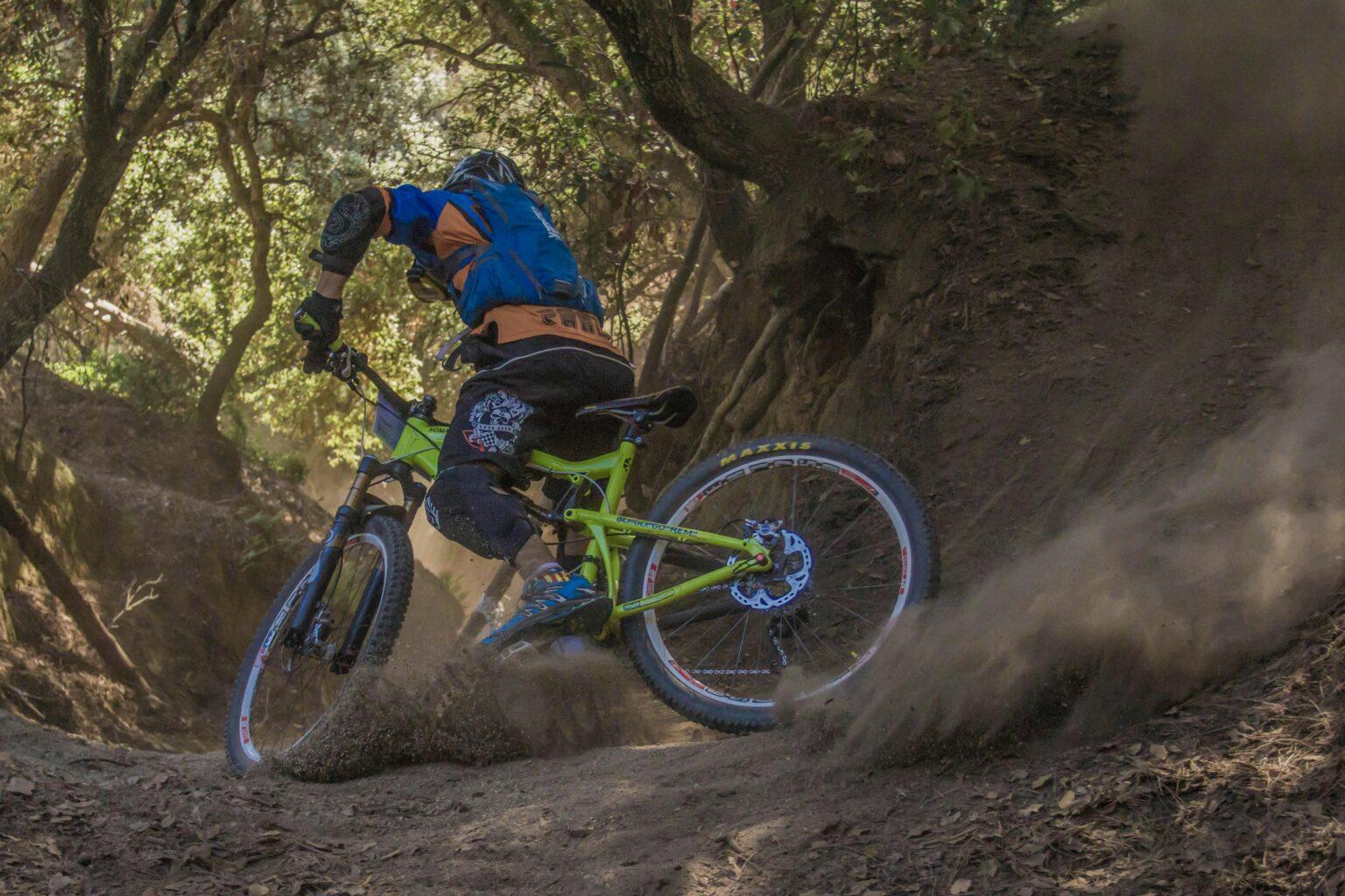 Mountain biker navigates a challenging off-road trail, kicking up dust in a forest setting.