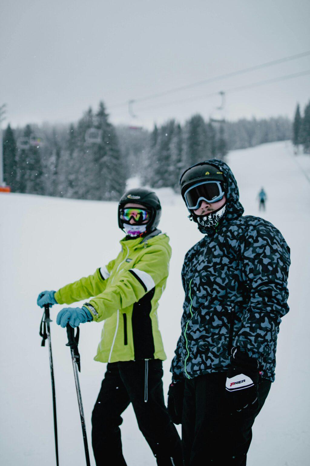 comment sélectionner des pantalons et salopettes pour le ski et le snowboard Anonymous couple in outerwear and ski equipment standing on snowy terrain near forest in winter time
