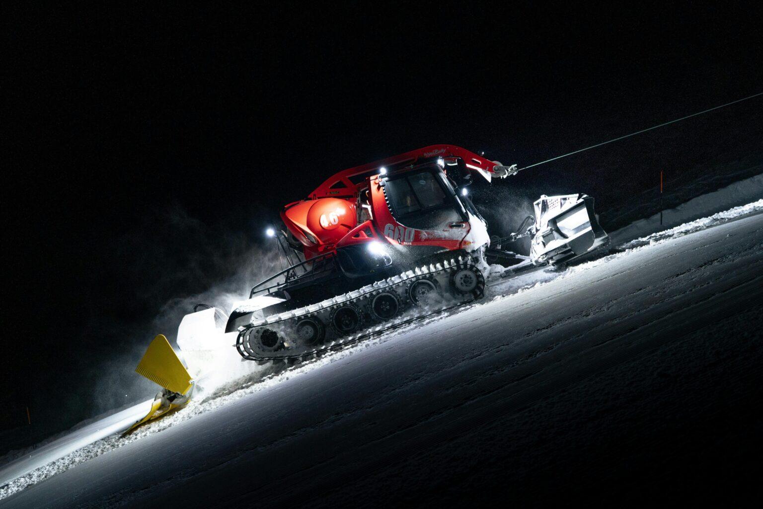 soin de base pour skis et snowboards DPS Phantom A snow groomer operates at night on a snowy slope in Zermatt, Switzerland.