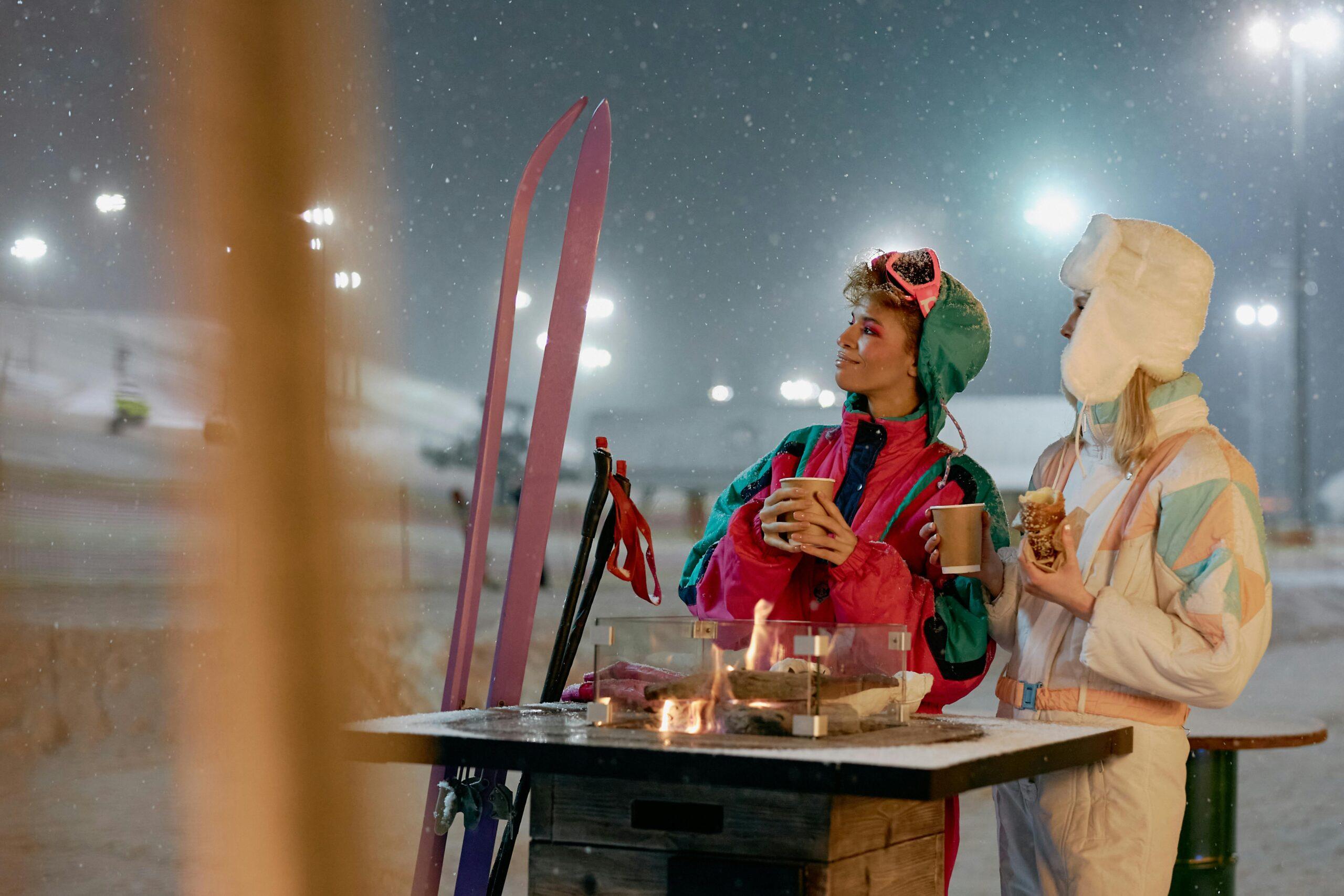 comment sélectionner des skis de randonnée alpine, AT ou de hors-piste Women enjoying warm beverages by a fire outdoors on a snowy winter night.