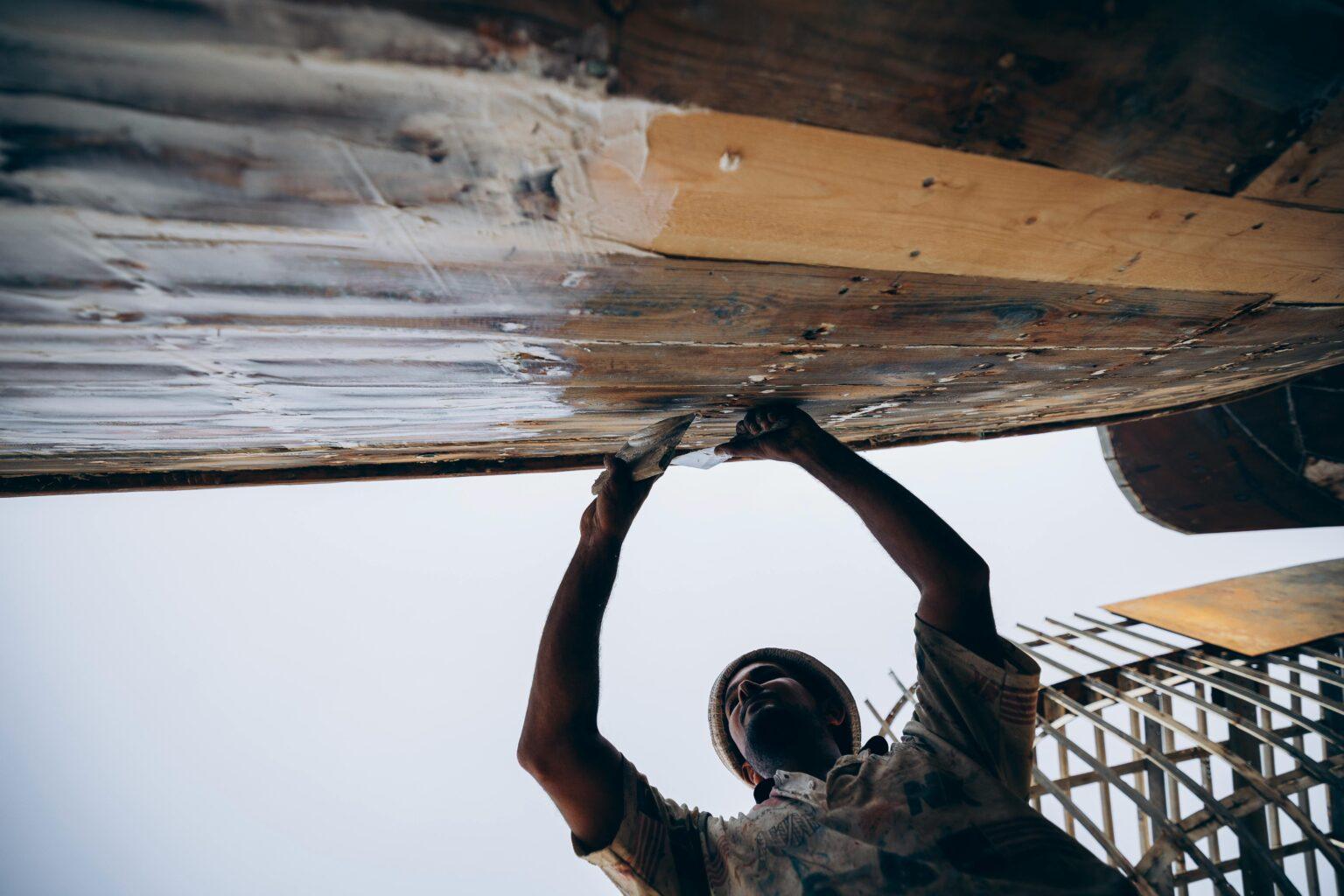 Réparer les déchirures de votre combinaison néoprène, l’entretenir et conseils de lavage A worker refurbishing a boat hull in Damietta, Egypt, captured in a dynamic street photography style.