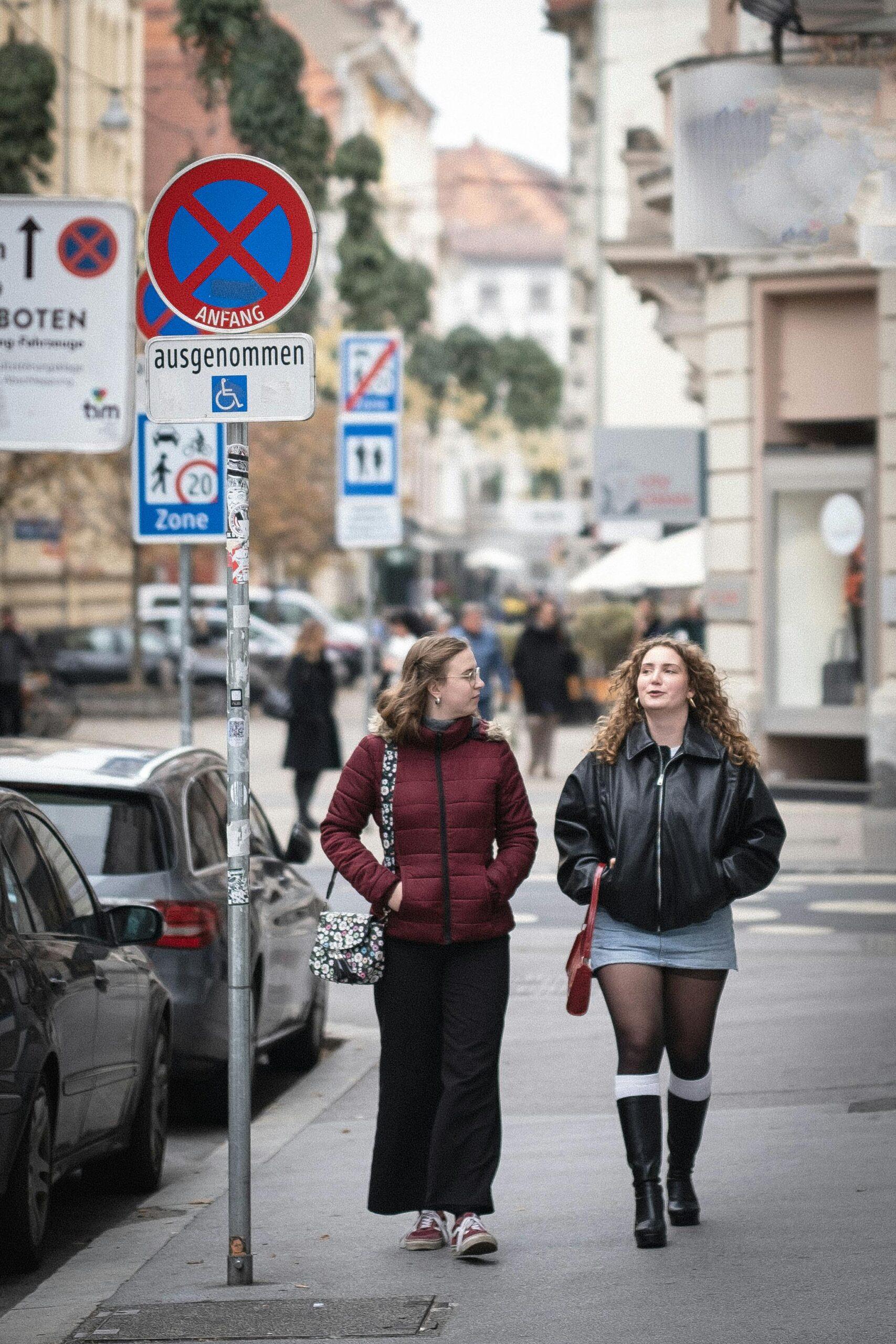 Two women walking and chatting on a bustling city street.
